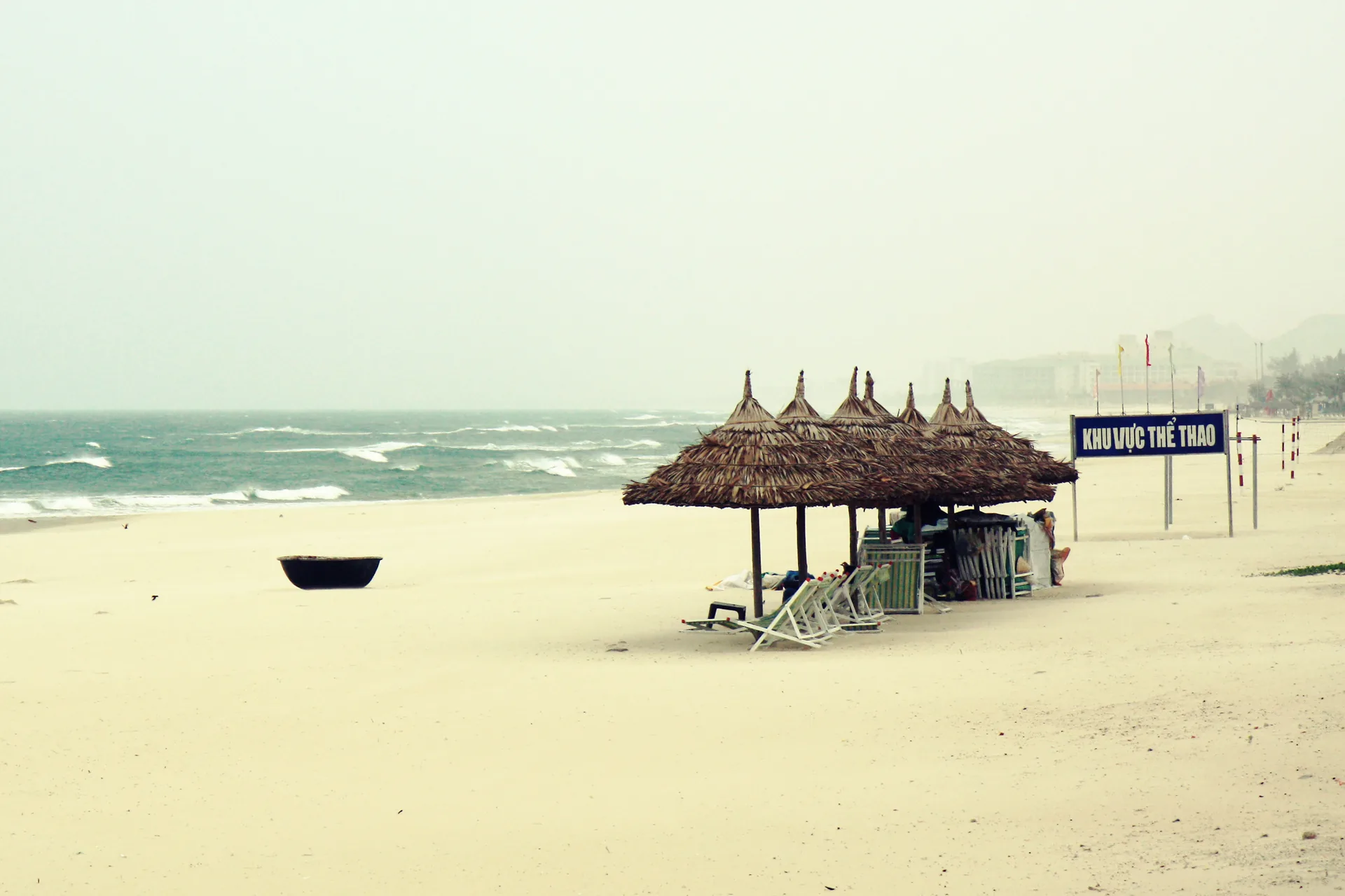 Thatched umbrellas, stacked loungers and a sports-area sign on a Da Nang beach