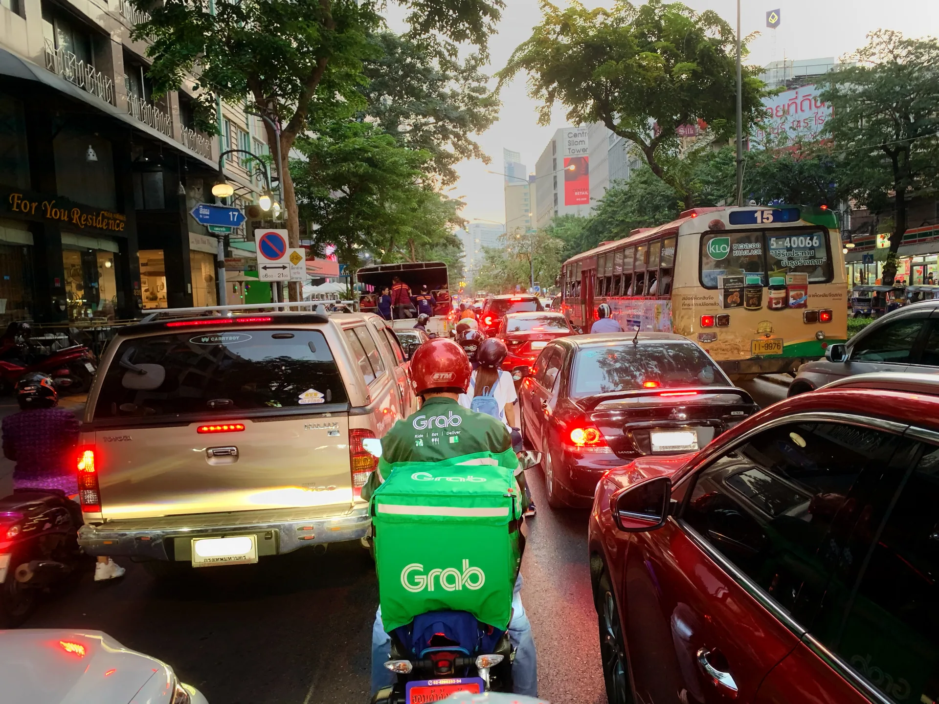 Курьер Grab с зелёным термокоробом едет на мотоцикле среди машин